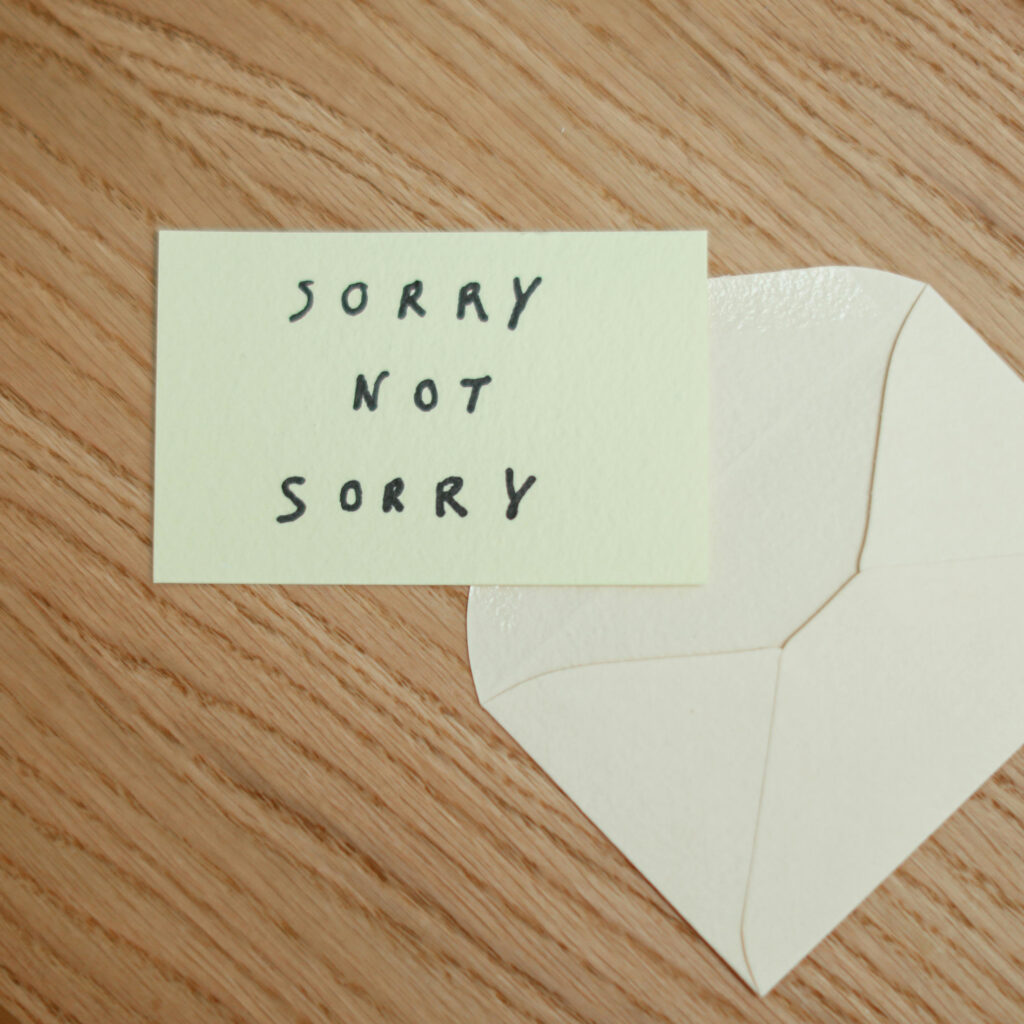 Imagebild zum Beitrag: Ein weißer Briefumschlag liegt auf einer Tischplatte aus Holz. Auf dem Umschlag liegt ein gelber Zettel mit den Worten "Sorry not sorry".