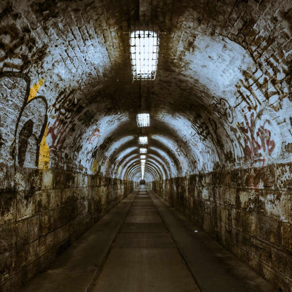 Imagebild zum Beitrag: Endlos wirkender düsterer Fußgängertunnel mit Graffitis an den Wänden.